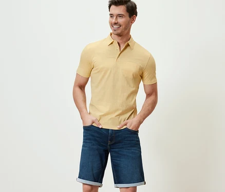 Mann posiert in gelb meliertem Jersey-Poloshirt und Jeansshorts.