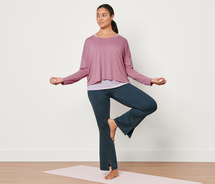 Frau in Baumpose auf Yogamatte trägt dunkelblaue Bodyforming-Sporthose und rosa 2-in-1-Sportshirt.