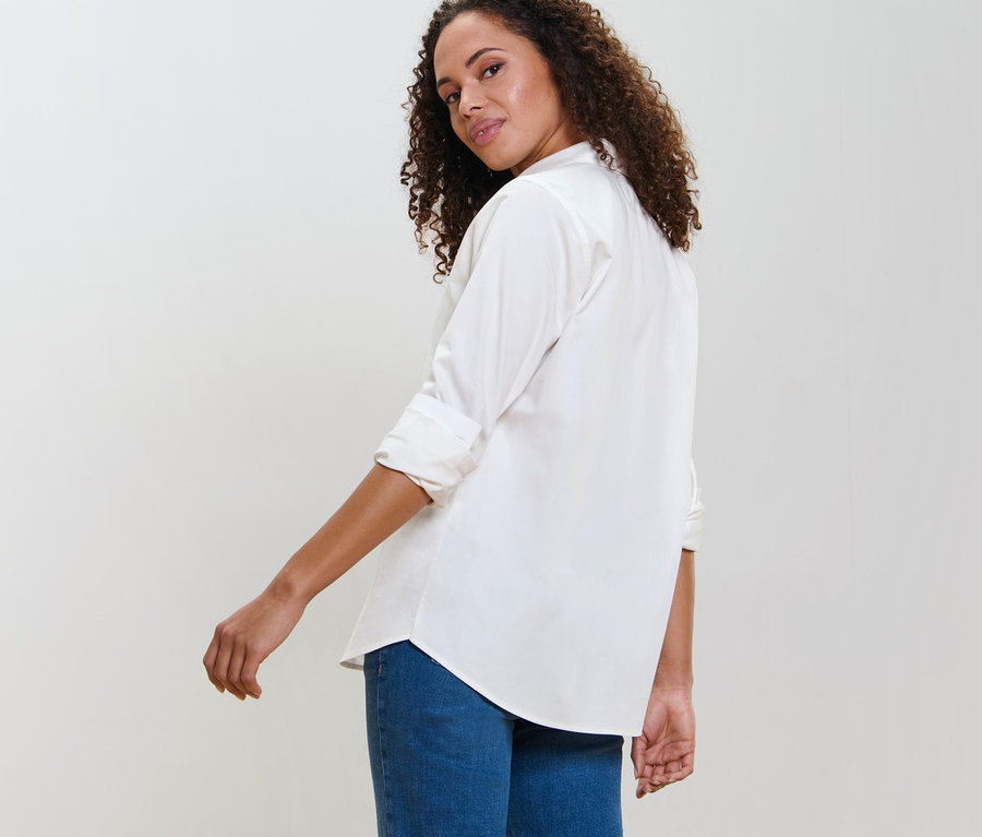 Frau blickt über die Schulter und trägt eine weiße Hemdbluse.