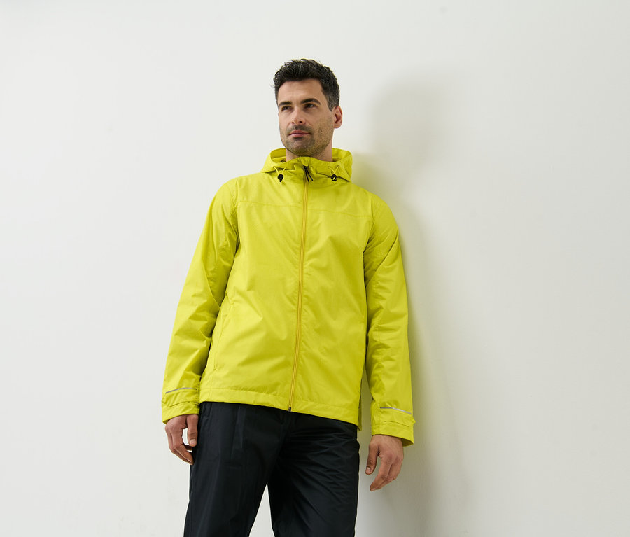 Mann lehnt an Wand und trägt gelbe Regenjacke.