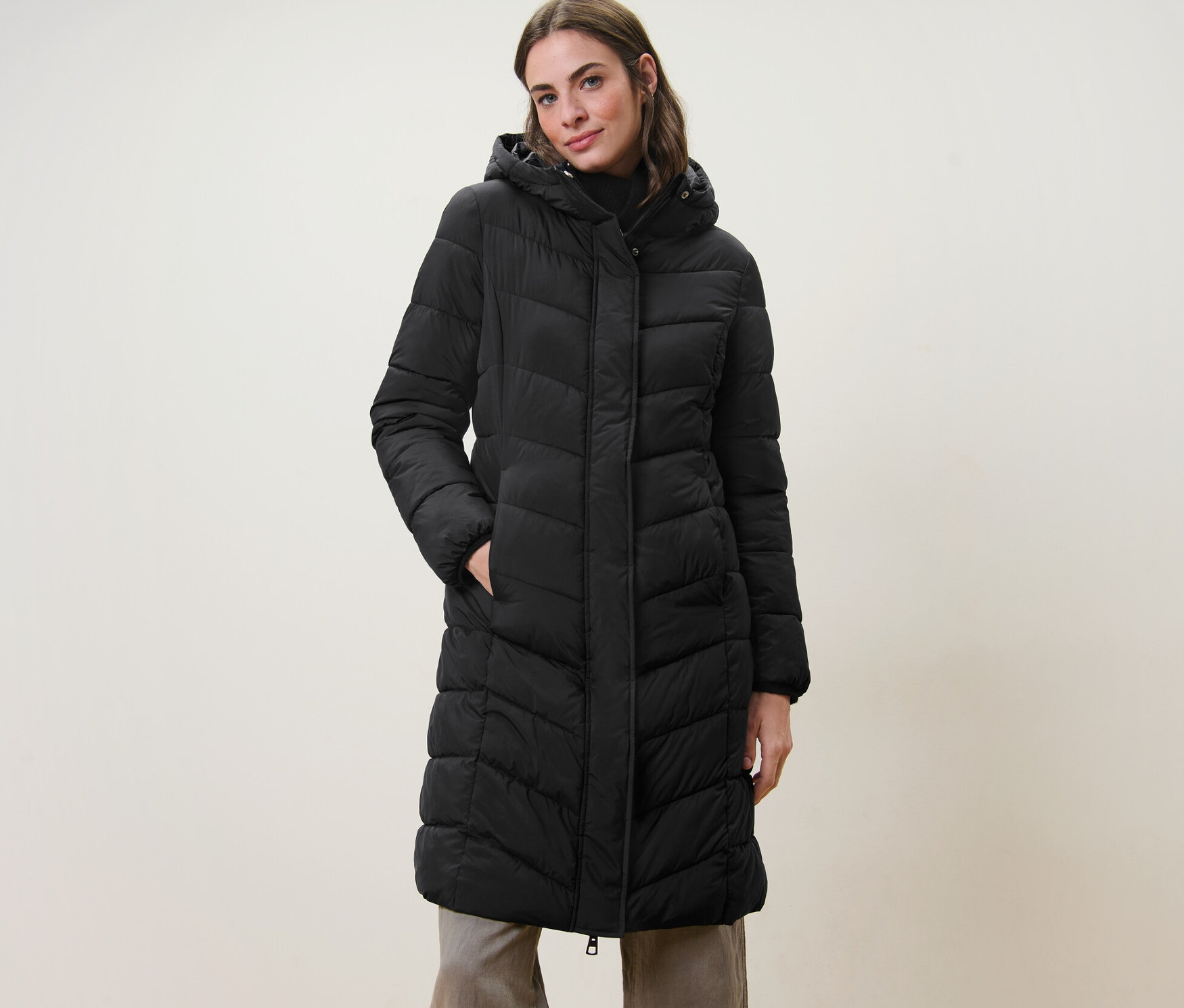 Frau posiert in einem schwarzen Steppmantel mit Kapuze.