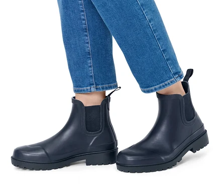 Beine in Jeans und Regenstiefeletten.