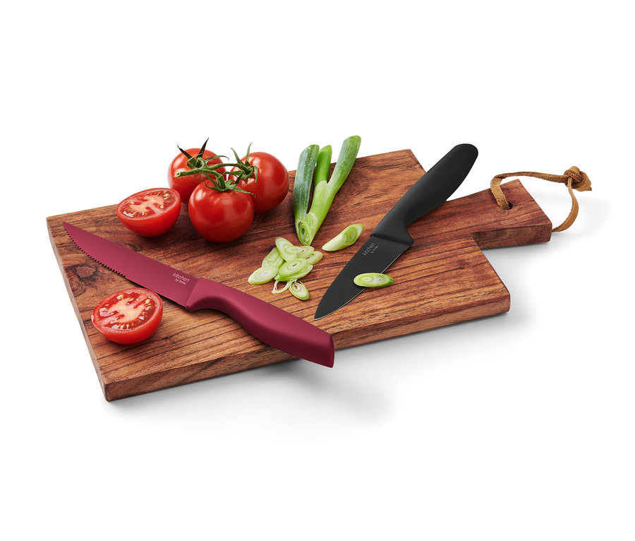 Auf einem Holzbrett liegen zwei Küchenmesser, Tomaten und geschnittene grüne Zwiebeln.