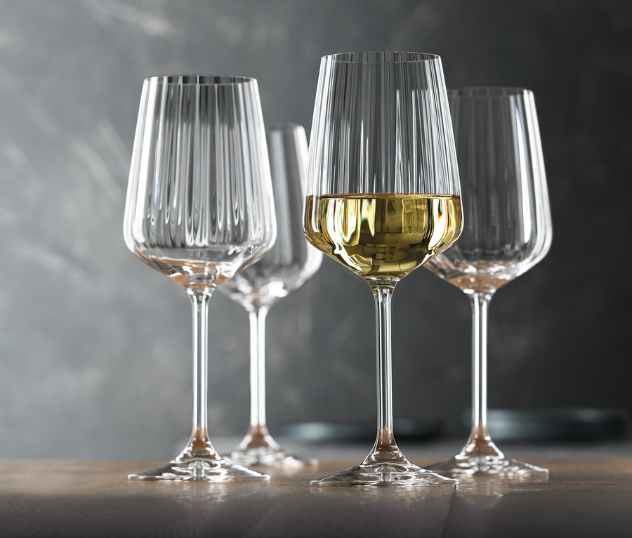 Vier Spiegelau Weißweingläser »Lifestyle« aus einem 8er-Set stehen auf einem Tisch, eines davon ist mit Weißwein gefüllt.