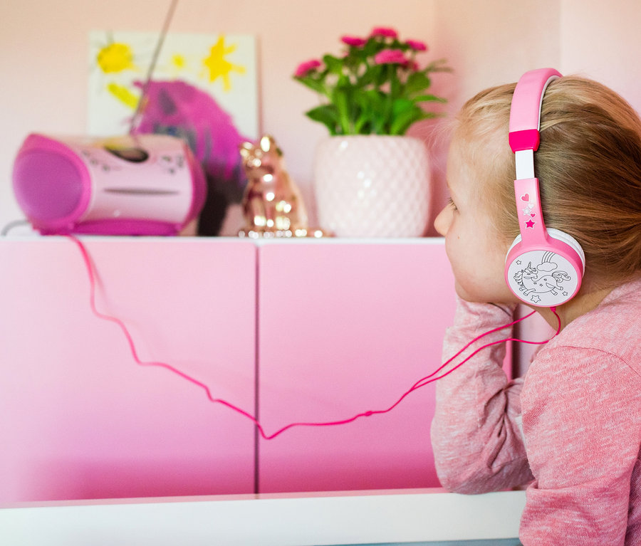 Mädchen hört Musik mit Kopfhörern. Auf dem Schrank stehen ein Radio, Deko und Blumen.