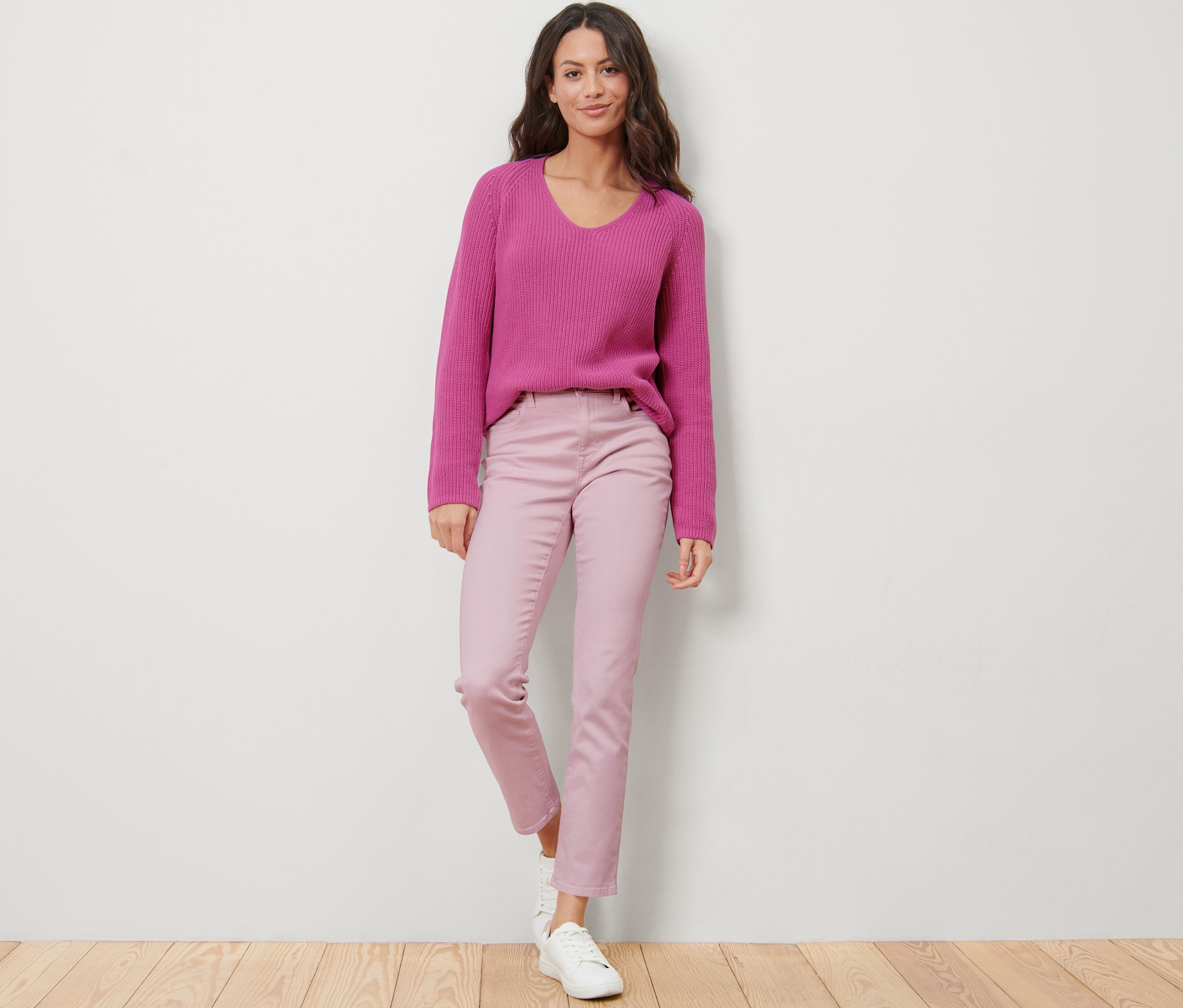 Eine Frau steht und trägt eine rosafarbene Jeans – Fit »Emma« und einen lila Pullover.