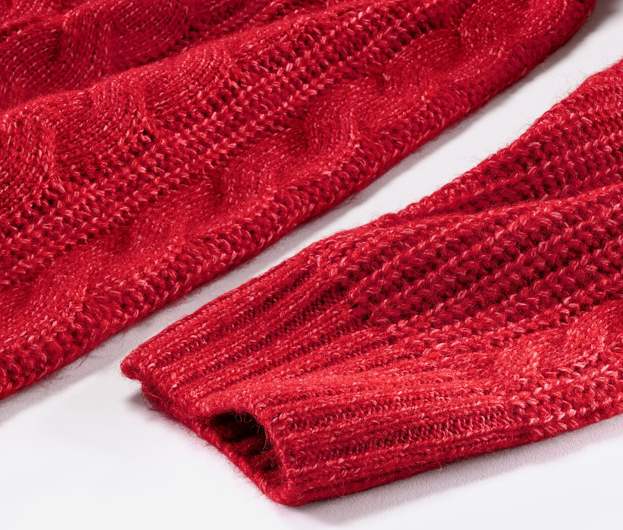Detailansicht eines langen, roten Strickpullovers mit Zopfmuster.