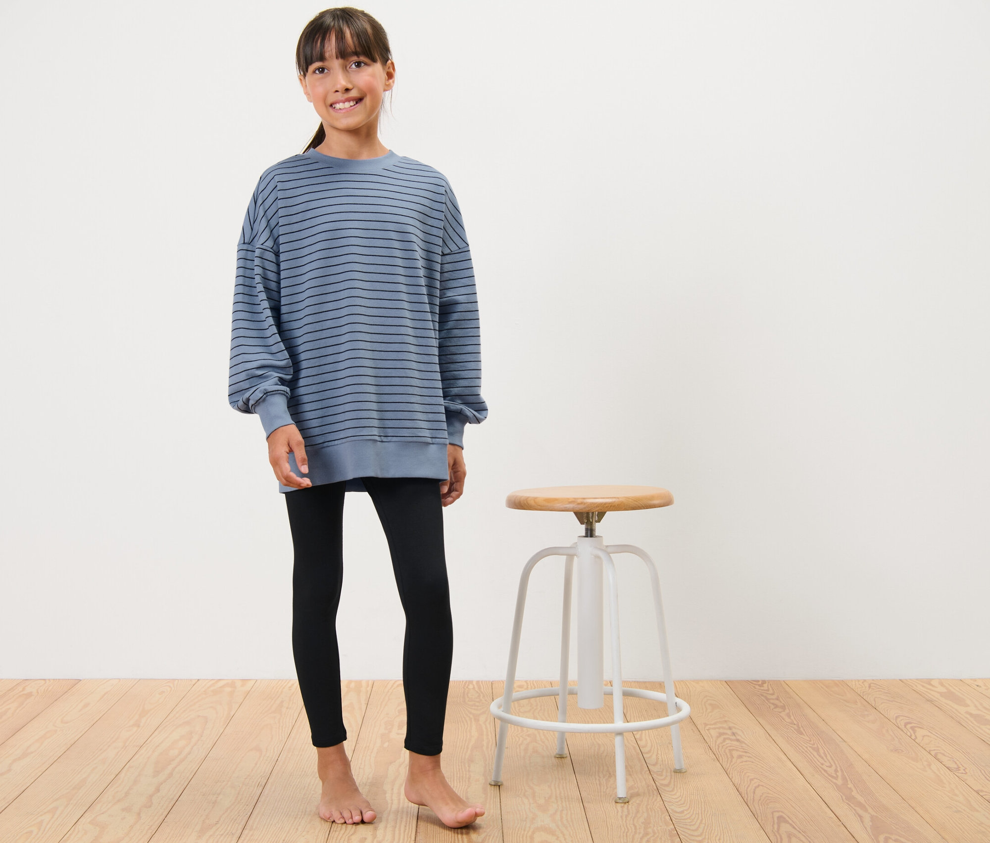 Mädchen im Kinder-Lounge-Pyjama posiert neben einem Hocker.