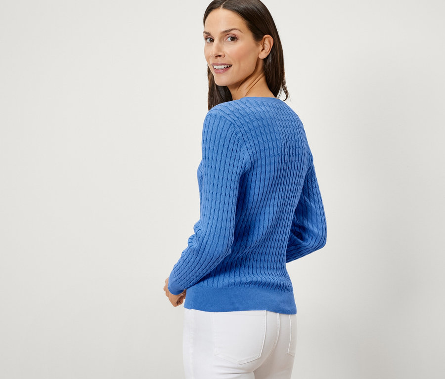 Eine Frau blickt über ihre Schulter und trägt einen blauen Zopfstrickpullover.