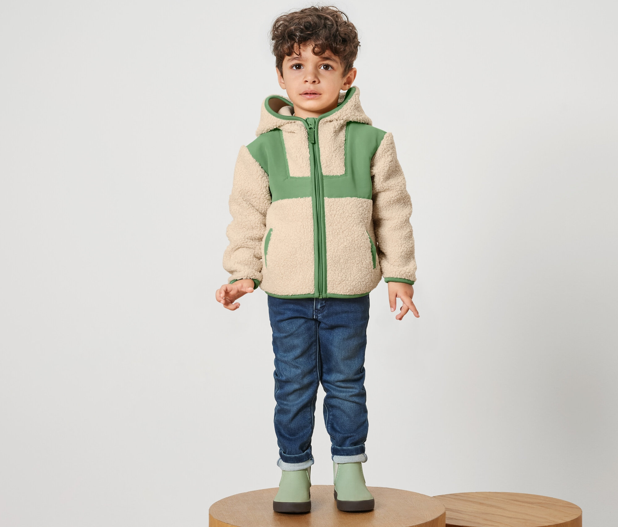 Ein Junge steht auf einem Sockel und trägt eine Kinder-Teddy-Jacke.