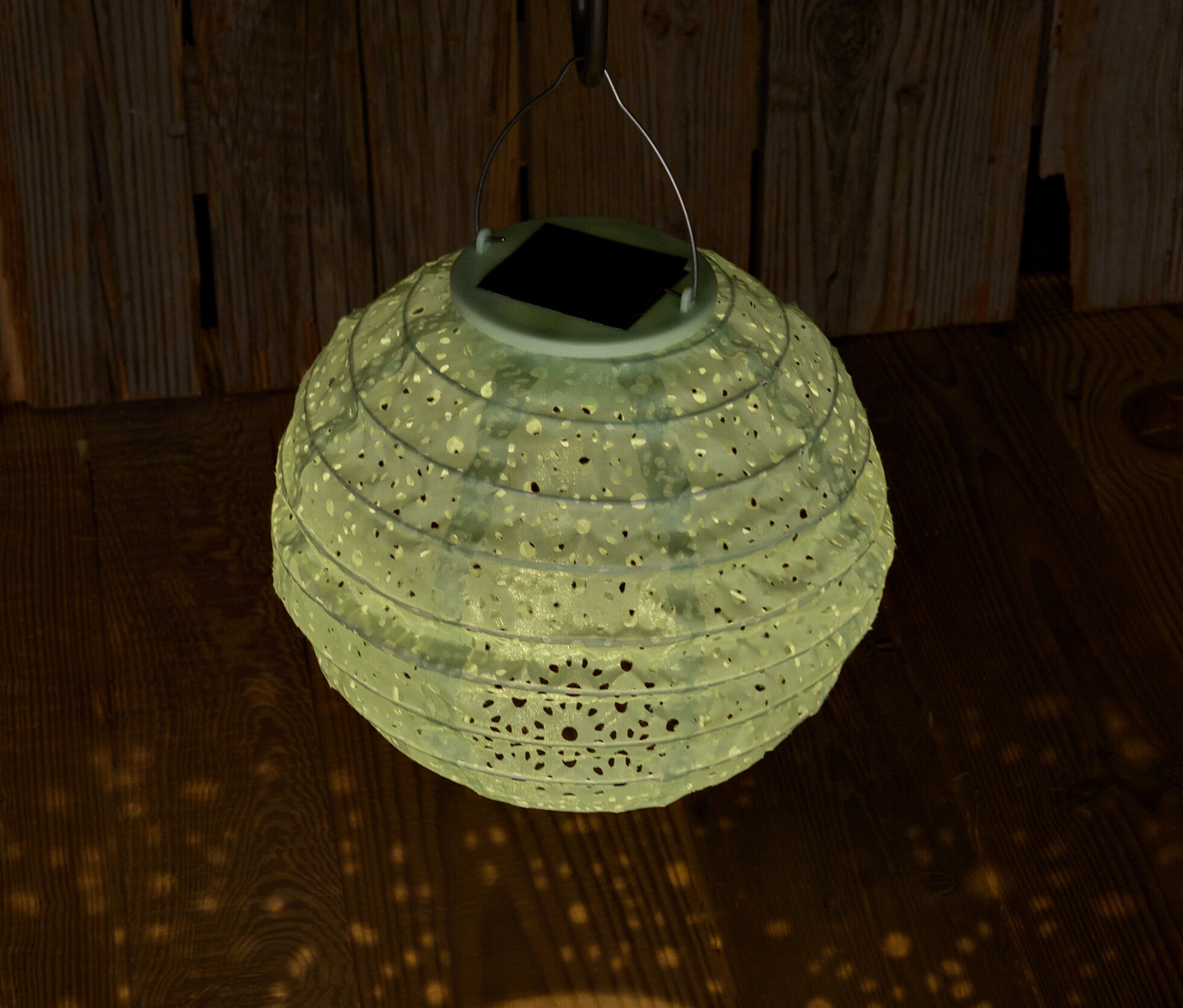 Hängende Solar-Lampion mit dekorativen Löchern projiziert Licht auf Holzboden.