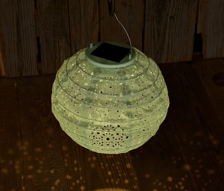 Hängende Solar-Lampion mit dekorativen Löchern projiziert Licht auf Holzboden.