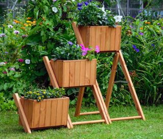 Eine braune Pflanztreppe mit 3 Pflanzkästen mit Blumen im Garten.