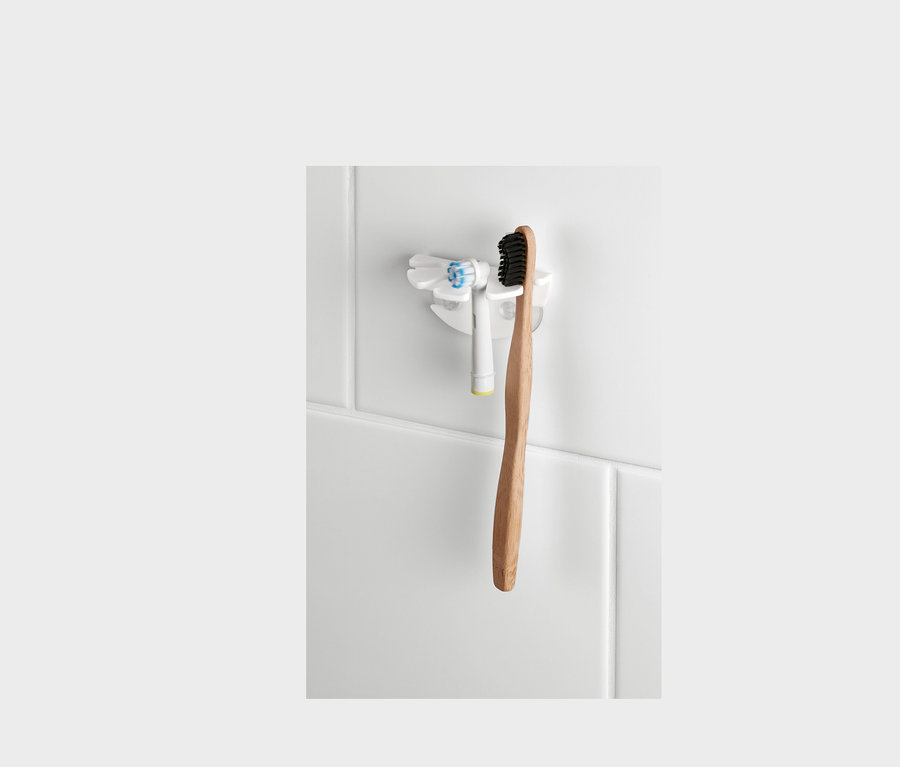 Ein Zahnbürstenhalter mit Saugnapf hält eine elektrische und eine Holzzahnbürste an weißen Fliesen.