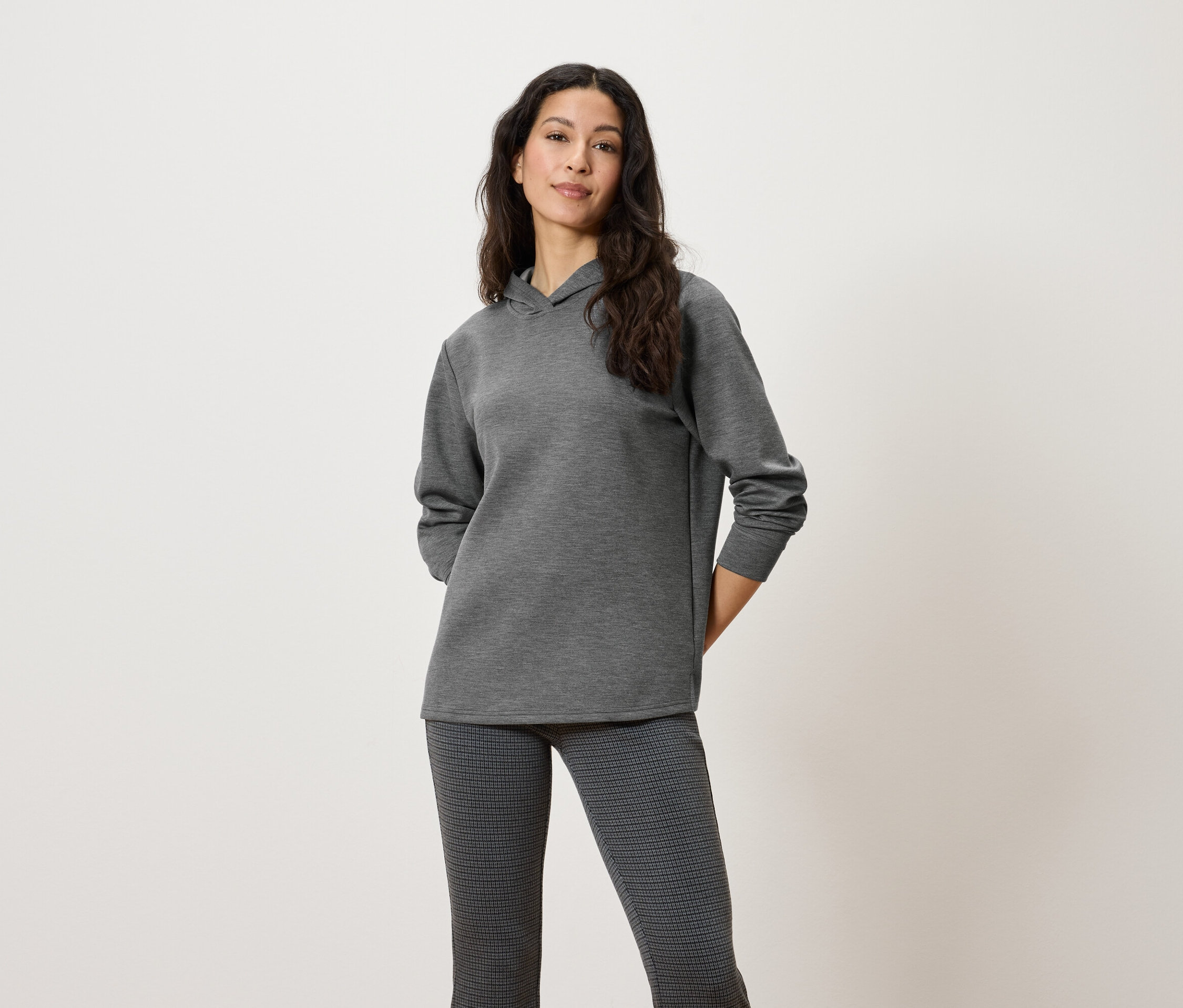 Frau posiert in einem grauen Kapuzenpullover und einer gemusterten Hose.