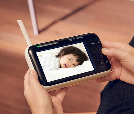 Eine Frau hält ein WiFi-Video-Babyphone »PIP1610« mit dem Bild eines liegenden Babys in der Hand.