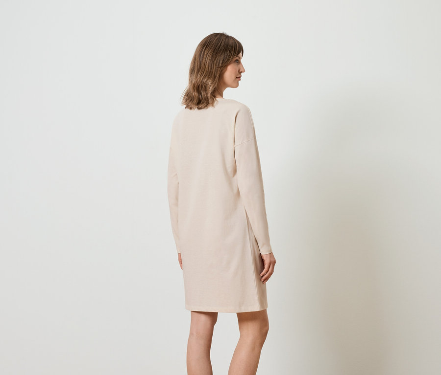 Frau trägt ein langes beiges Kleid, von hinten gesehen.