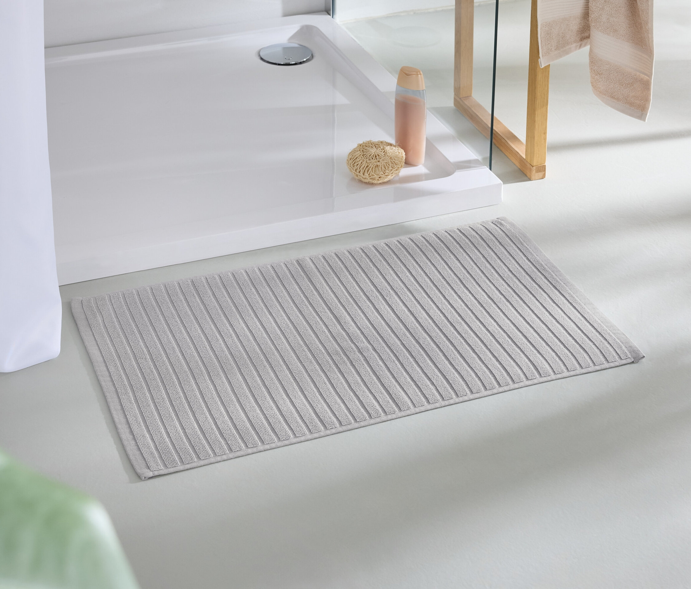 Eine beige Badematte liegt auf dem Boden neben einer Dusche.