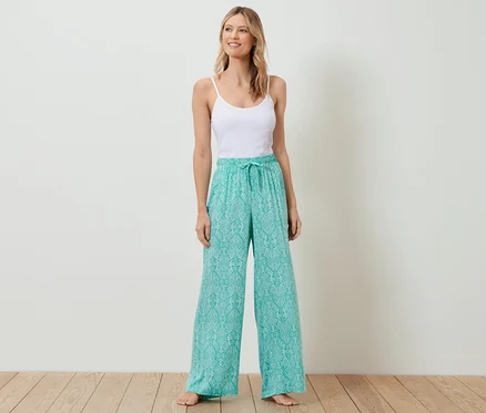 Frau steht und trägt ein weißes Top und eine Relaxhose.