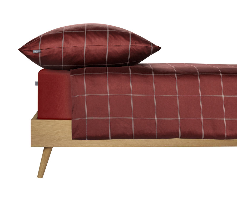 Nahaufnahme eines Bettes mit rot karierter SCHIESSER Satin-Bettwäsche »Josh« in Normalgröße und einem passenden Kissen auf einem hellen Holzrahmen.