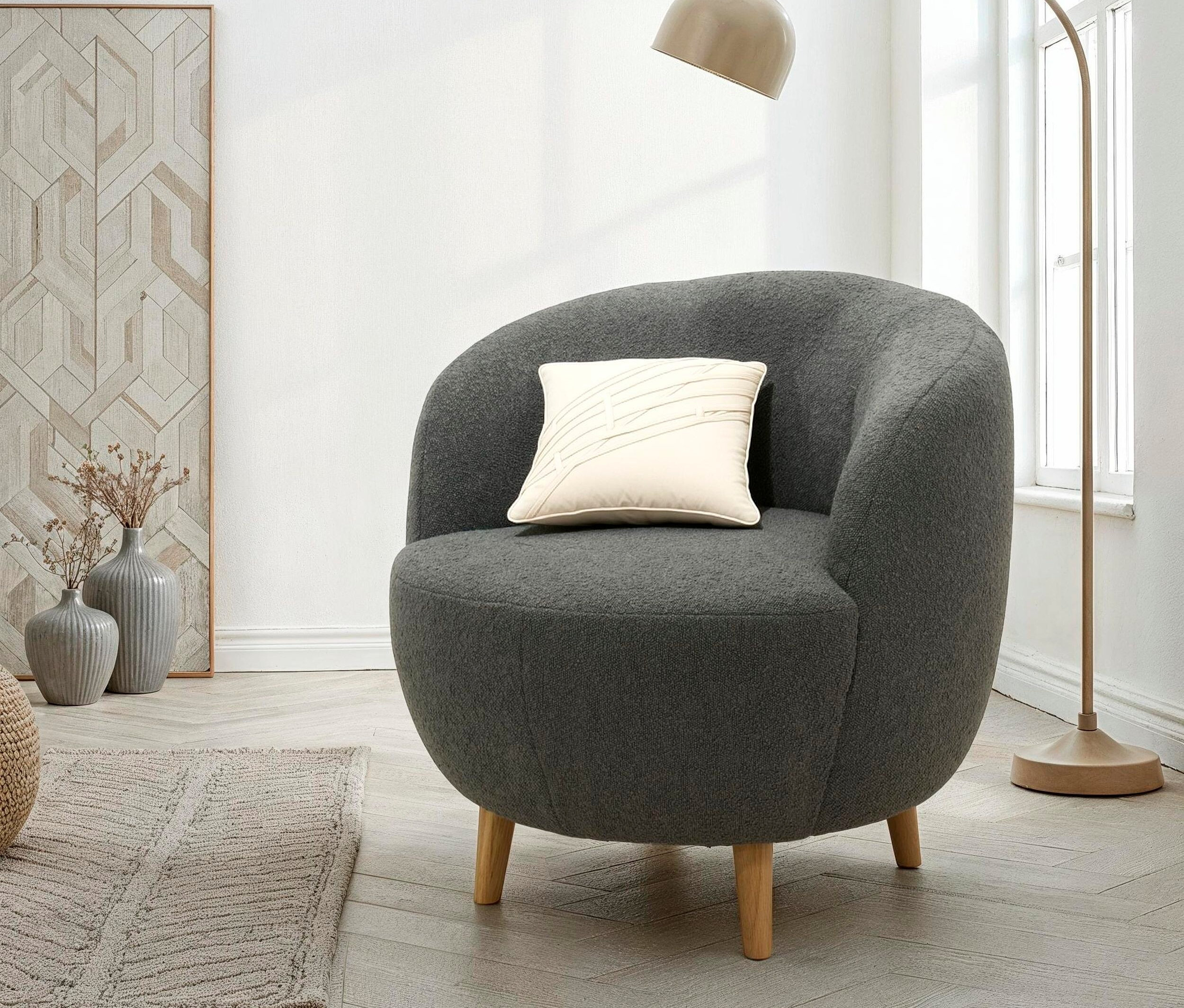 Ein grauer Sessel mit einem cremefarbenen Kissen steht neben einer Bogenlampe.