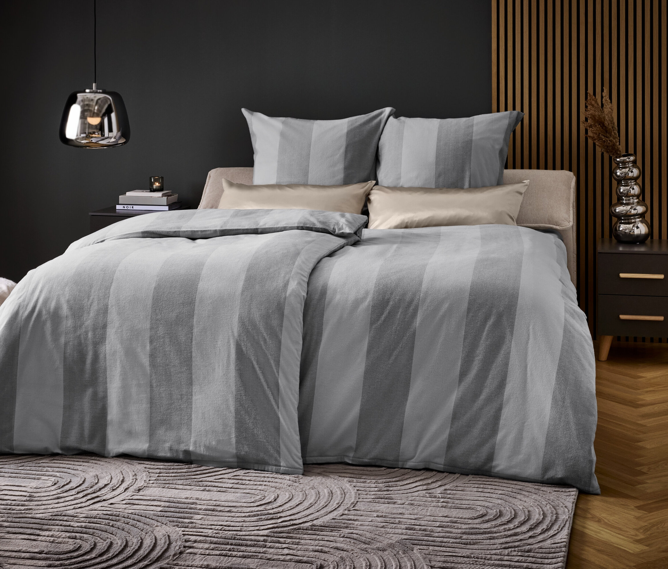 Schlafzimmer mit einem Bett mit grau gestreifter Bettwäsche, zwei Kissen und einem Nachttisch.