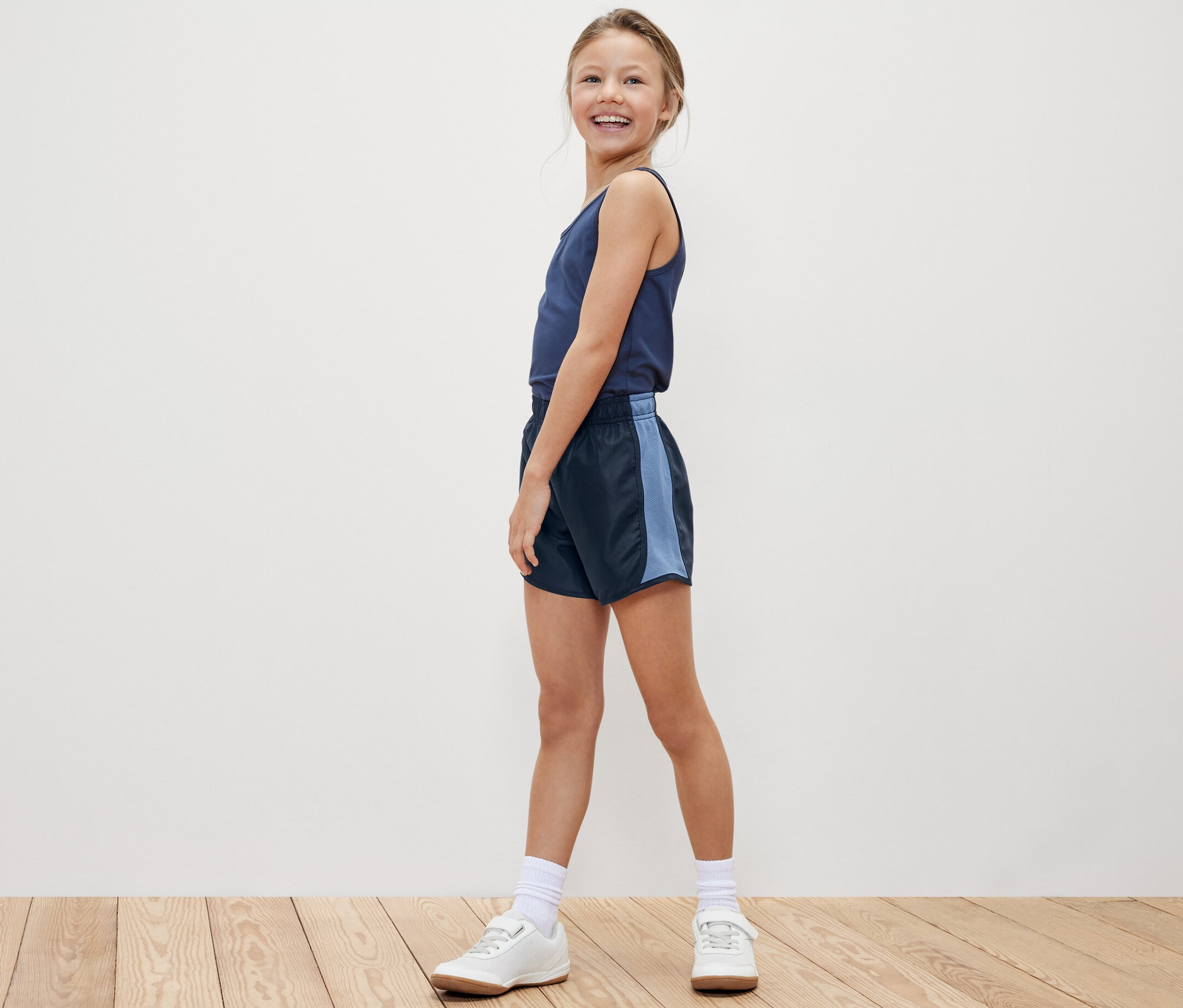 Lächelndes Mädchen posiert in Tanktop und einer der 2 Kinder-Sportshorts.
