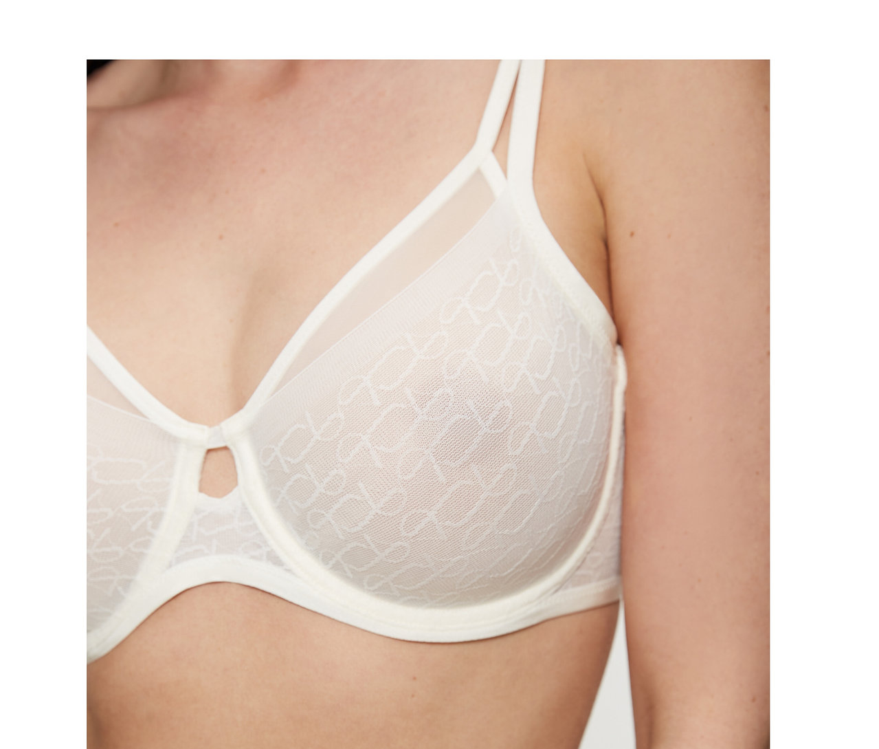 Frau trägt einen cremeweißen Triumph Signature Sheer Minimizer BH mit gemusterten, transparenten Cups und einem kleinen Schlüssellochausschnitt in der Mitte.