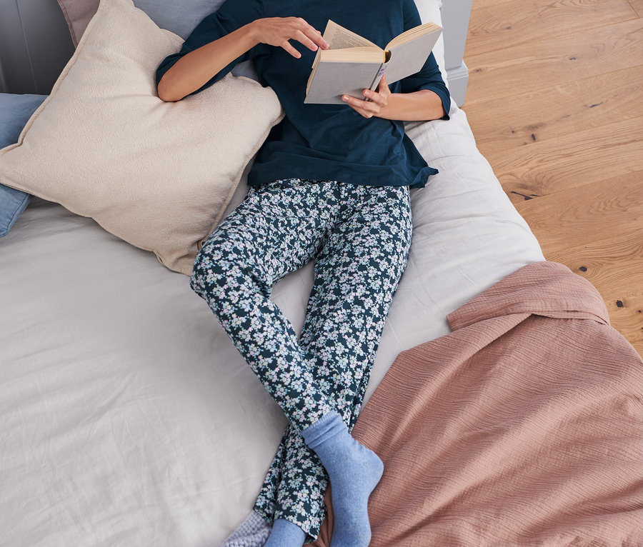 Frau liegt im Bett und liest ein Buch. Sie trägt einen Pyjama.