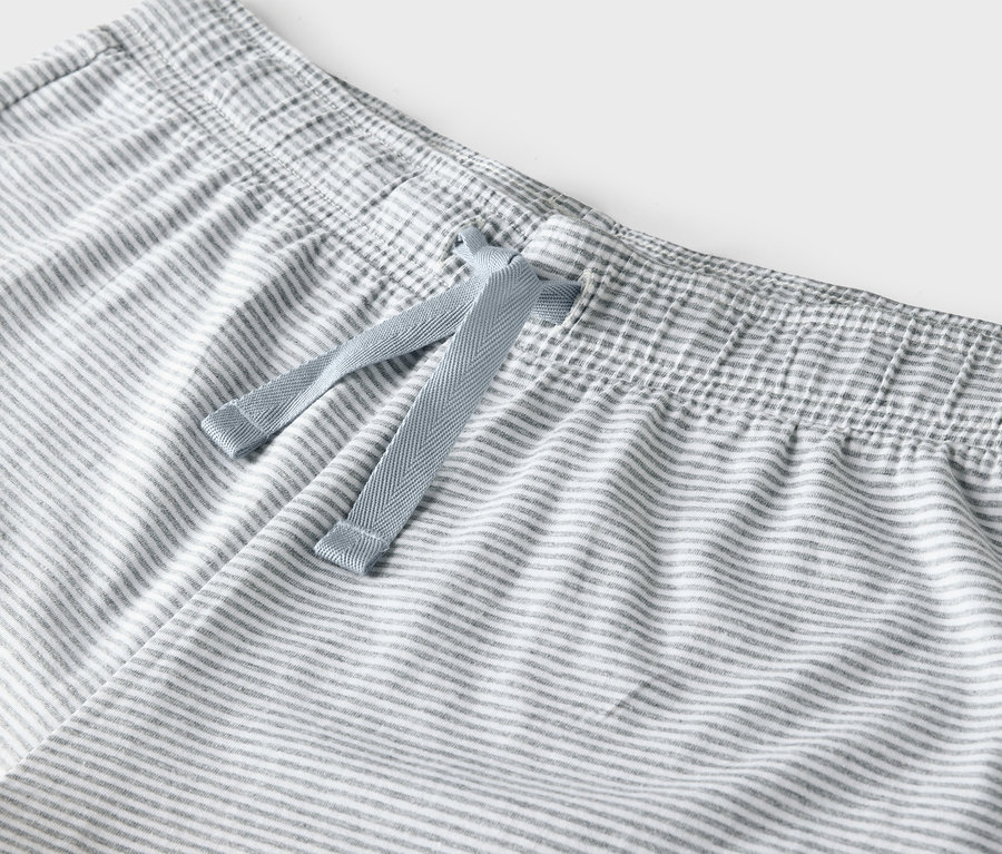 Detail einer grau-weiß gestreiften Hose mit blauem Kordelzug in der Taille.
