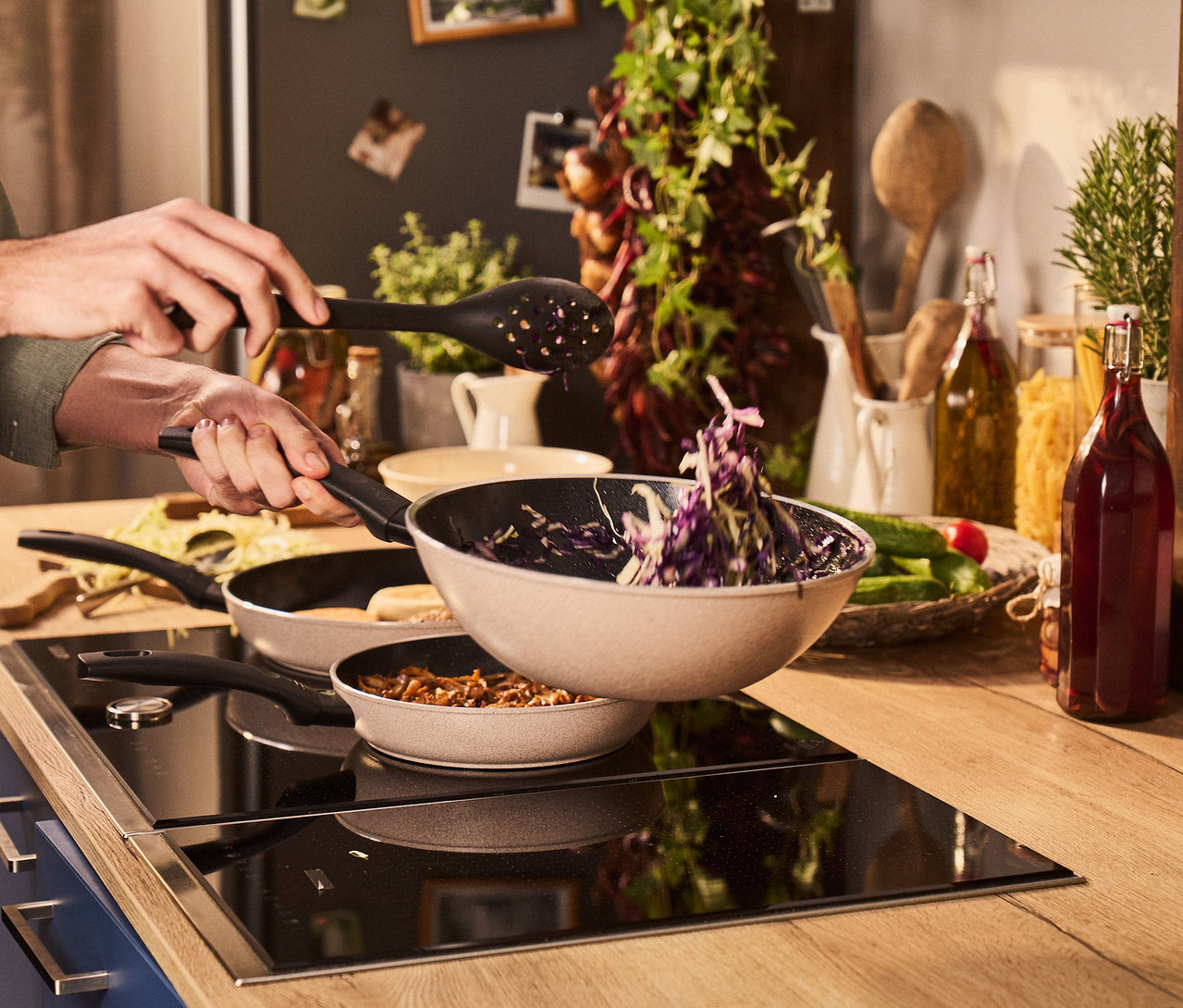 Eine Person kocht mit einem BALLARINI Ledro Wok (28 cm) auf einem Herd, wobei sie Gemüse in den Wok gibt.