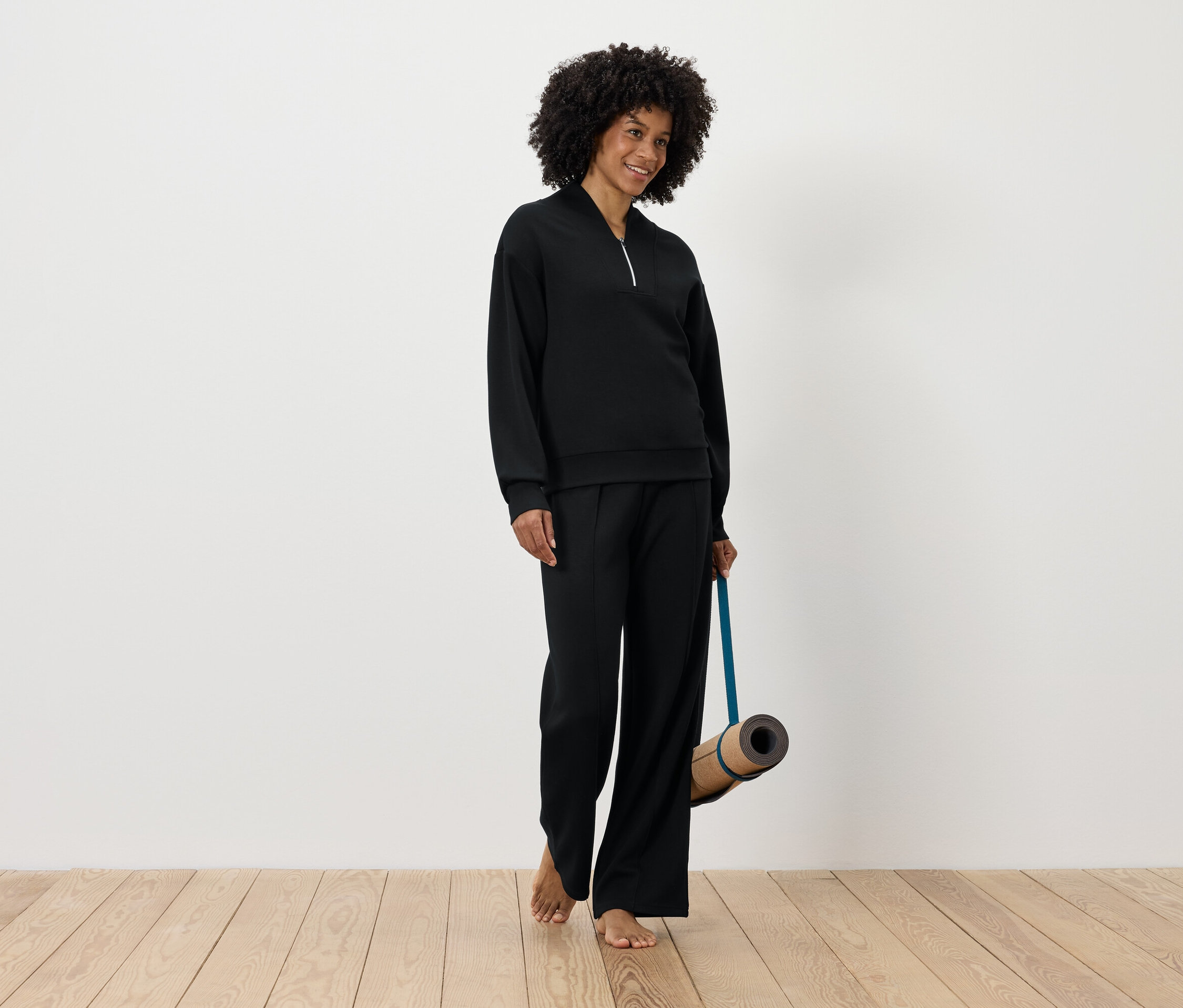 Frau in schwarzer Sportbekleidung hält eine Yogamatte.