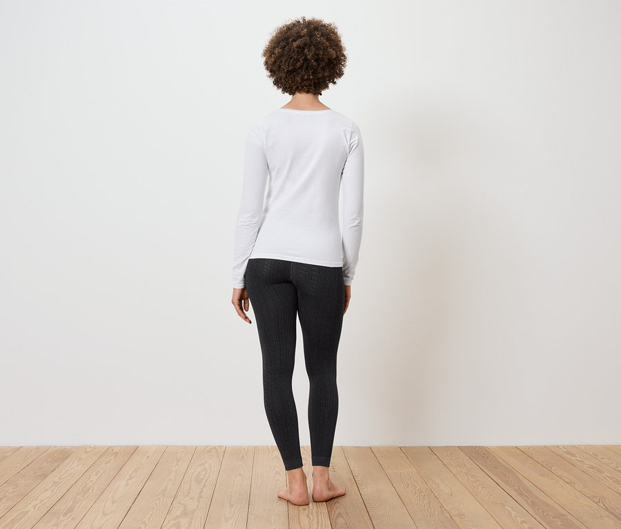 Frau mit Afro-Frisur steht mit dem Rücken zur Kamera und trägt ein weißes Langarmshirt und schwarze Leggings.