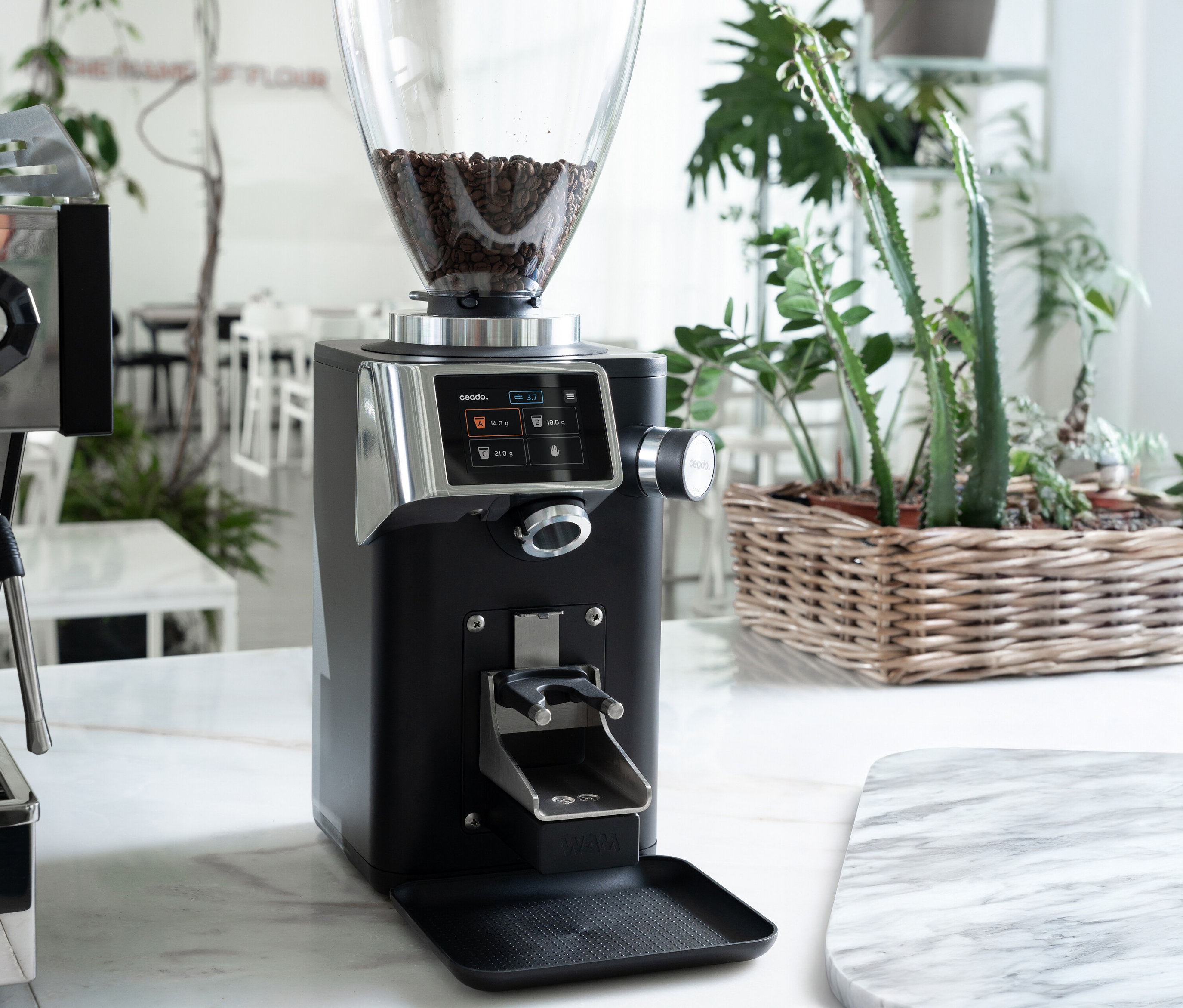 Eine schwarze Kaffeemühle mit Bohnen im Trichter steht auf einer Marmoroberfläche.