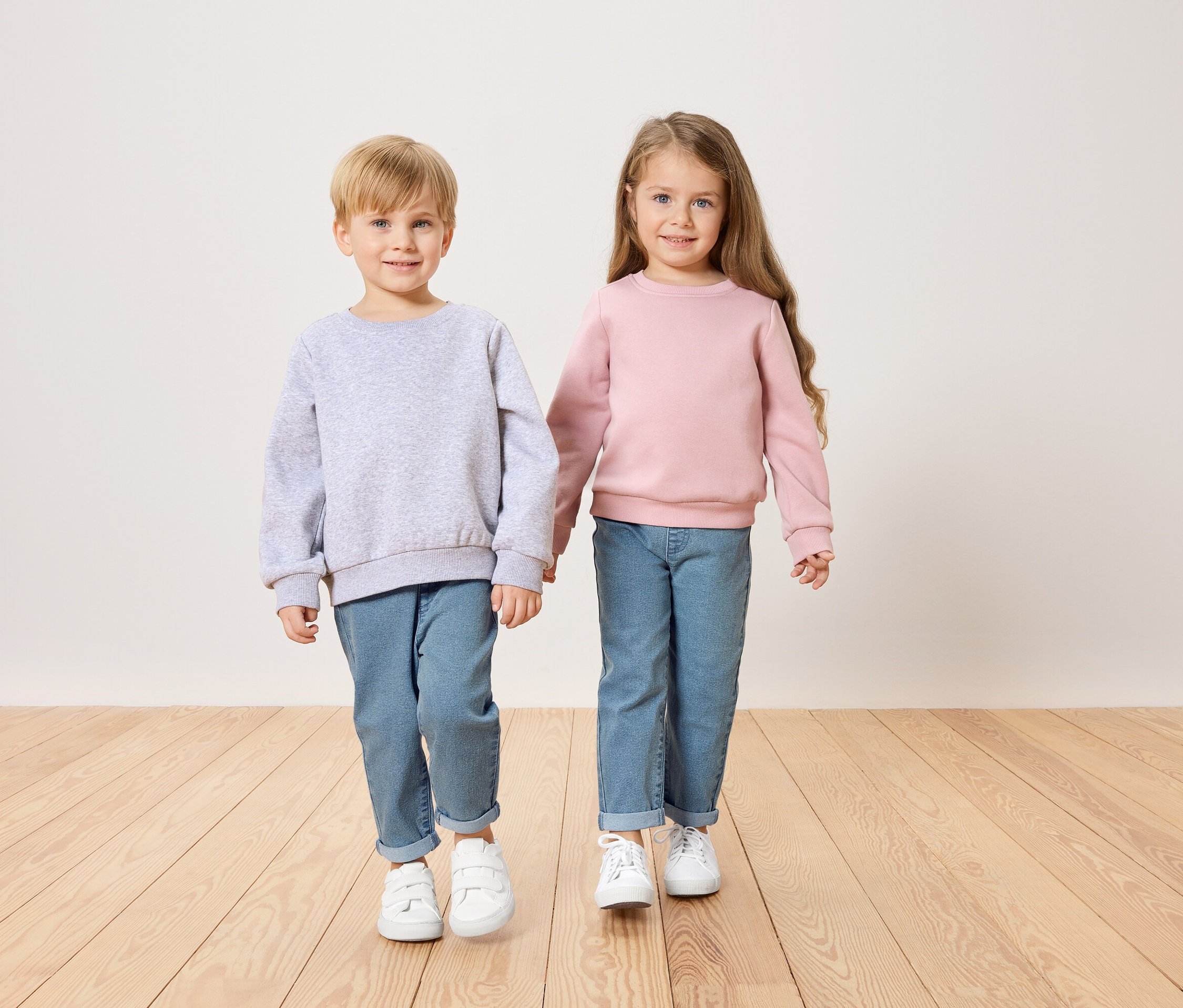 Ein Junge im grauen Pullover und ein Mädchen im rosa Pullover halten Händchen.