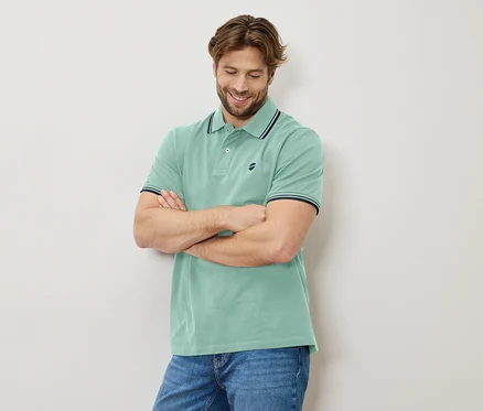 Mann mit verschränkten Armen, trägt ein hellgrünes Poloshirt und Jeans.