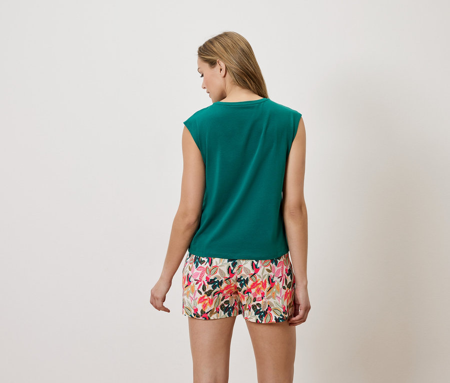 Rückansicht einer Frau mit blonden Haaren, die ein grünes, ärmelloses Oberteil und Shorts mit Blumenmuster trägt.