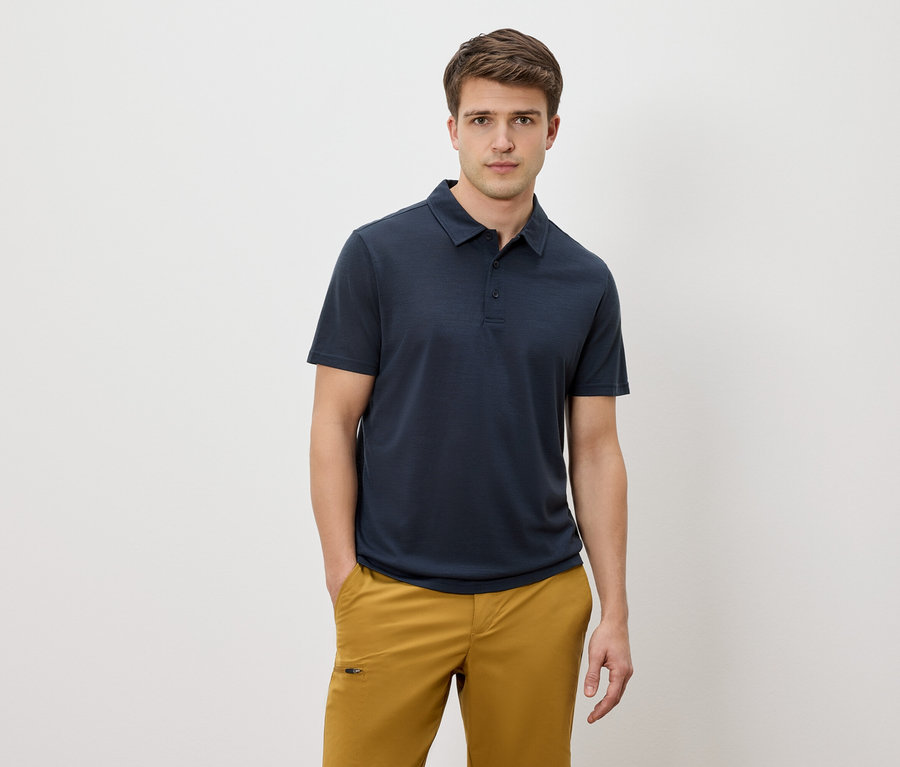 Mann mit blauem Poloshirt und gelben Hosen vor einem weißen Hintergrund.