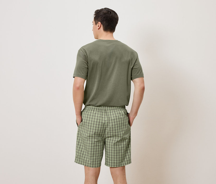 Ein Mann mit dem Rücken zur Kamera trägt ein grünes T-Shirt und Shorts mit grünem Karomuster.