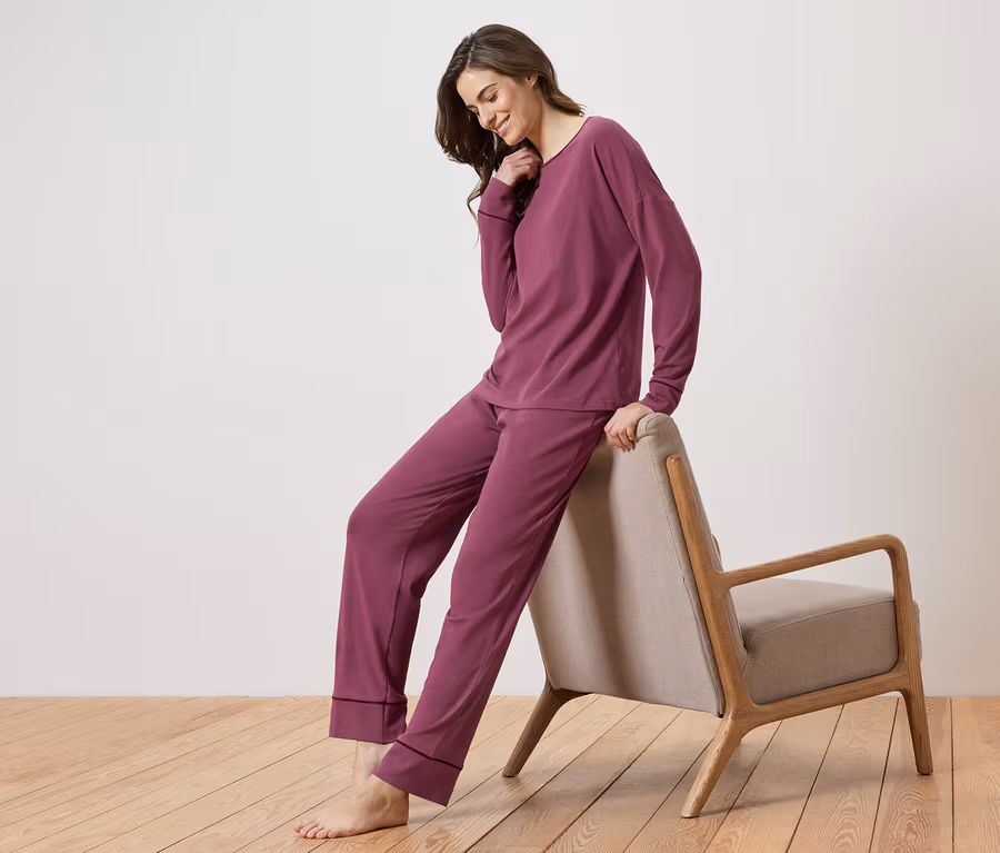 Frau in einem auberginefarbenen Pyjama-Set, die sich an einen Stuhl lehnt.