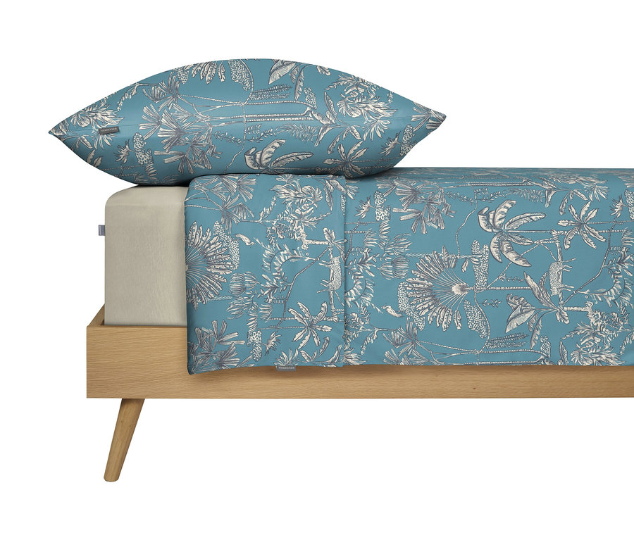 Bett mit blauem Bettbezug und Kissen mit weißem tropischen Pflanzenmuster.