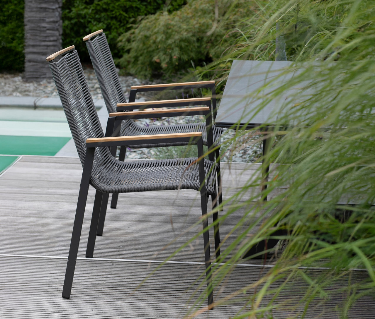 Zwei graue Stühle mit Holzarmlehnen stehen auf einer Holzterrasse neben einem Tisch.