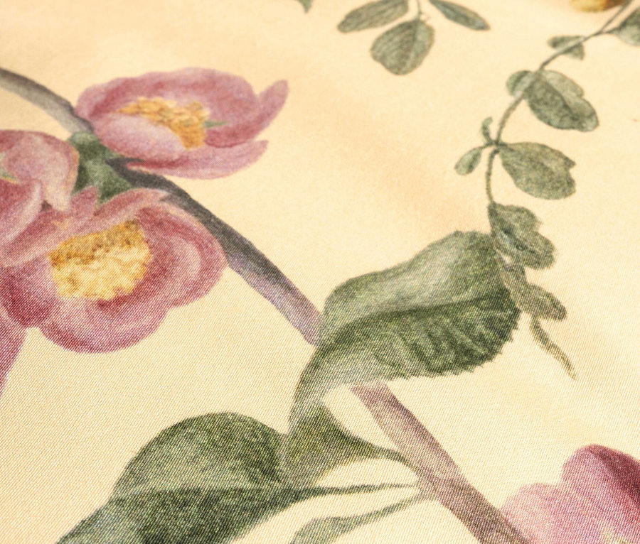 Nahaufnahme eines Stoffes mit Blumenmuster in Rosa und Grün auf beigem Hintergrund.