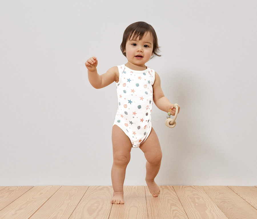 Ein Baby steht auf einem Holzboden und hält ein Spielzeug in der Hand.