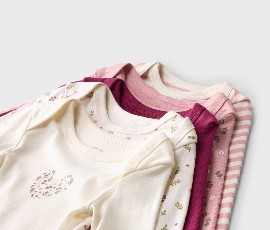 Stapel aus fünf Babybodys in Weiß, Rosa und Lila mit verschiedenen Blumenmustern und Streifen.