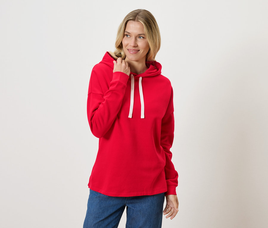 Eine Frau trägt einen roten Hoodie und Jeans.