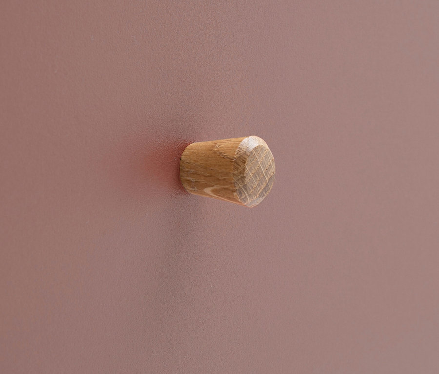 Nahaufnahme eines hölzernen Schubladengriffs an einer rosafarbenen Oberfläche.