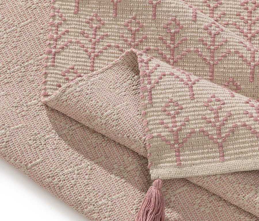 Nahaufnahme eines gefalteten Teppichs mit rosa Baum-Muster und Quaste.