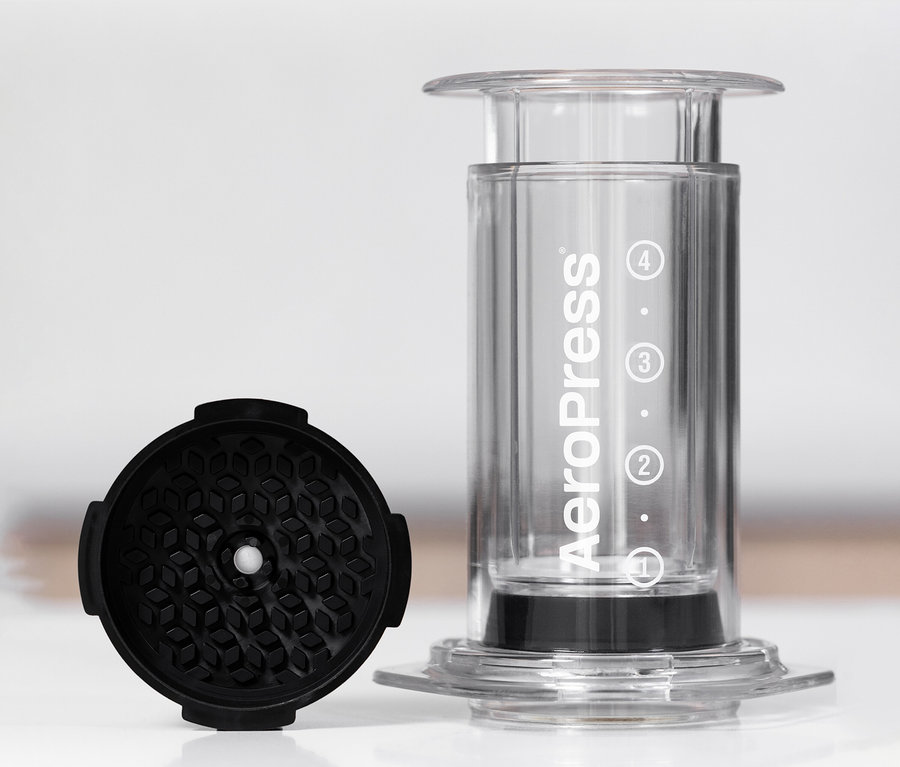 Durchsichtiger AeroPress Coffee Maker »Clear« steht neben einem schwarzen Zubehörteil.