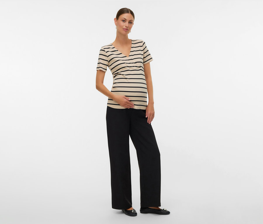 Frau mit Umstands-T-Shirt »MLLANE TESS« mit schwarzen Streifen, schwarzen Hosen und flachen Schuhen, Hand auf dem Bauch.
